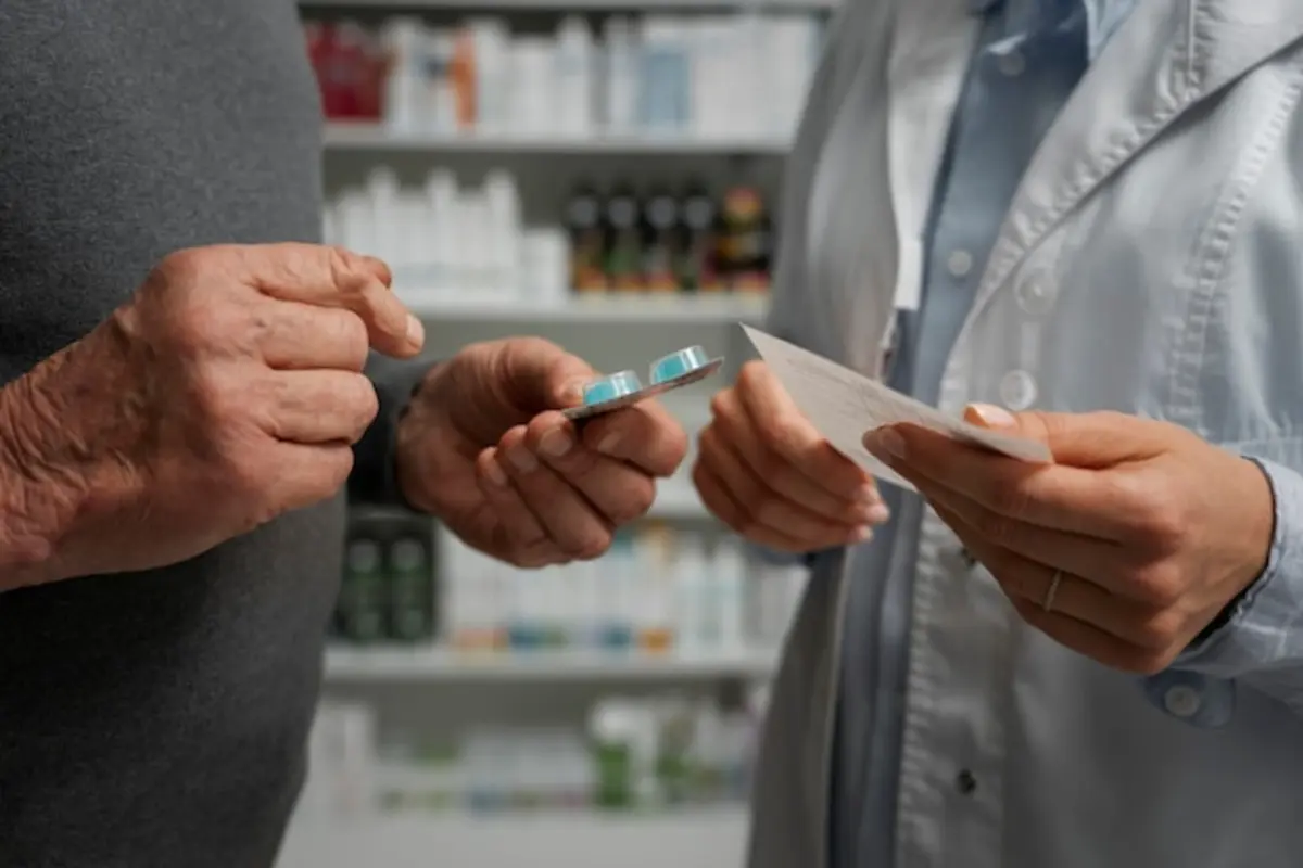 Farmacêutico entregando cartela de medicamento a paciente idoso ao balcão da farmácia