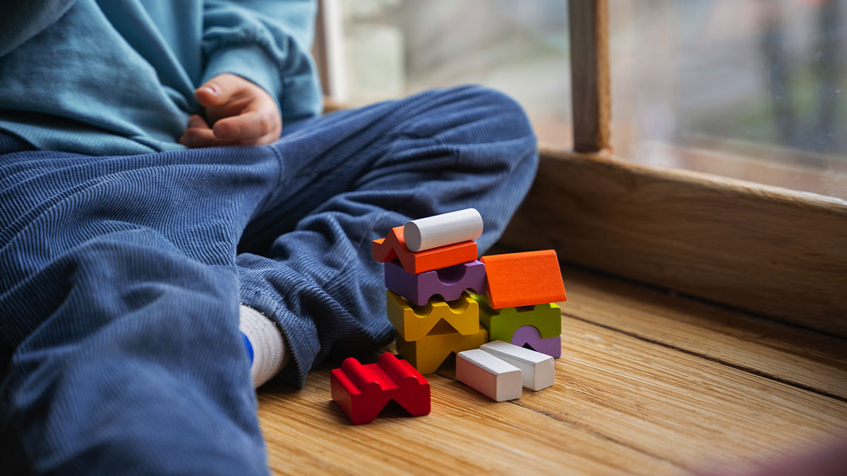 Criança com autismo brincando com blocos coloridos próximos à janela