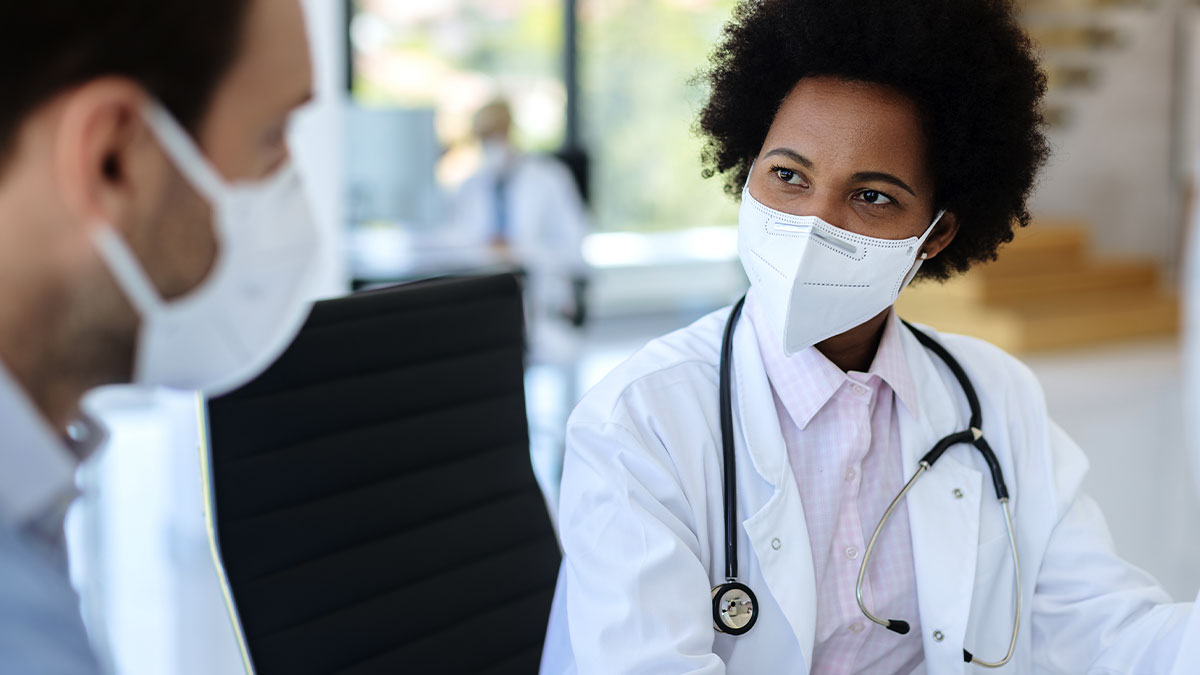 Médica com máscara de proteção orientando paciente sobre direitos de cobertura de quimioterapia no plano de saúde.