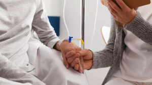 Paciente em sessão de quimioterapia segurando a mão de acompanhante